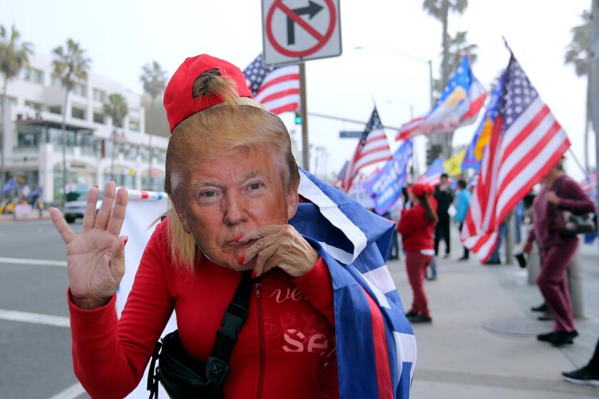 President Donald Trump supporter holds a mask of the commander-in-chief during election rally at the Huntington Beach pier in Huntington Beach on Wednesday, Jan. 6, 2020. About 200 people waves flags, played musis and danced in support of President Donald Trump.