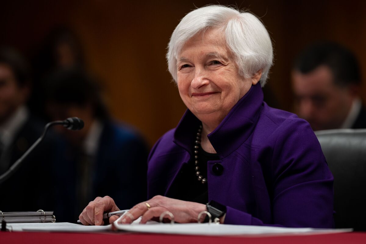 Secretary of the Treasury Janet Yellen sits at a table before a microphone.