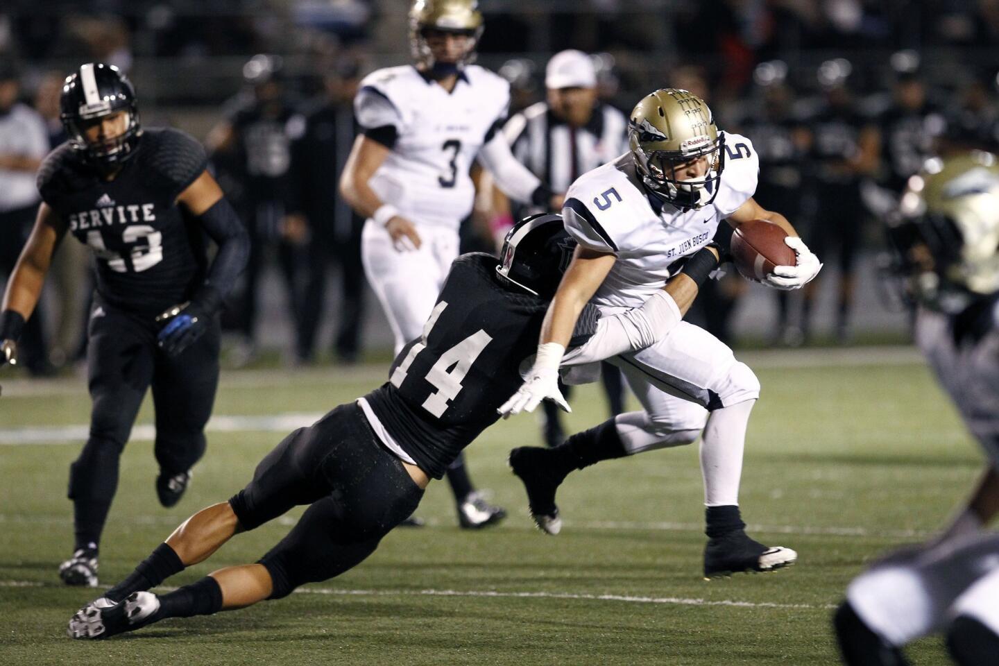 St. John Bosco running back Sean McGrew, right, tries to avoid a tackle by Servite's Nico Ament during the Braves' 49-26 win Friday.