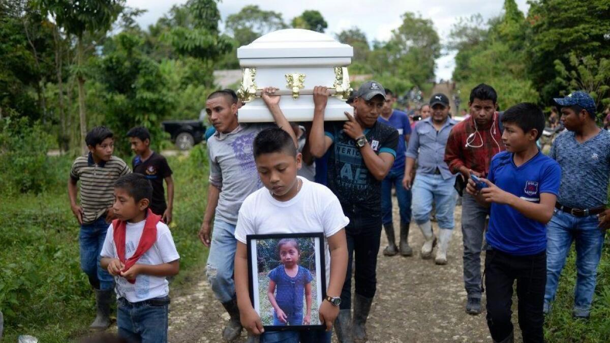A boy carries a picture of Jakelin Caal, a 7-year-old who died after being taken into custody by the U.S. Border Patrol last month, as her coffin is taken for burial in Guatemala. On Dec. 24, another child migrant from Guatemala died in the U.S.