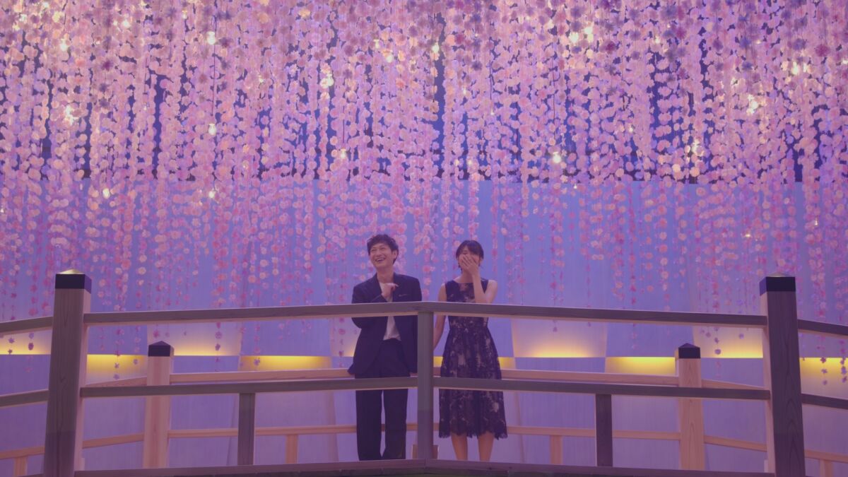 A couple stands on a bridge in a space decorated in purple and pink.