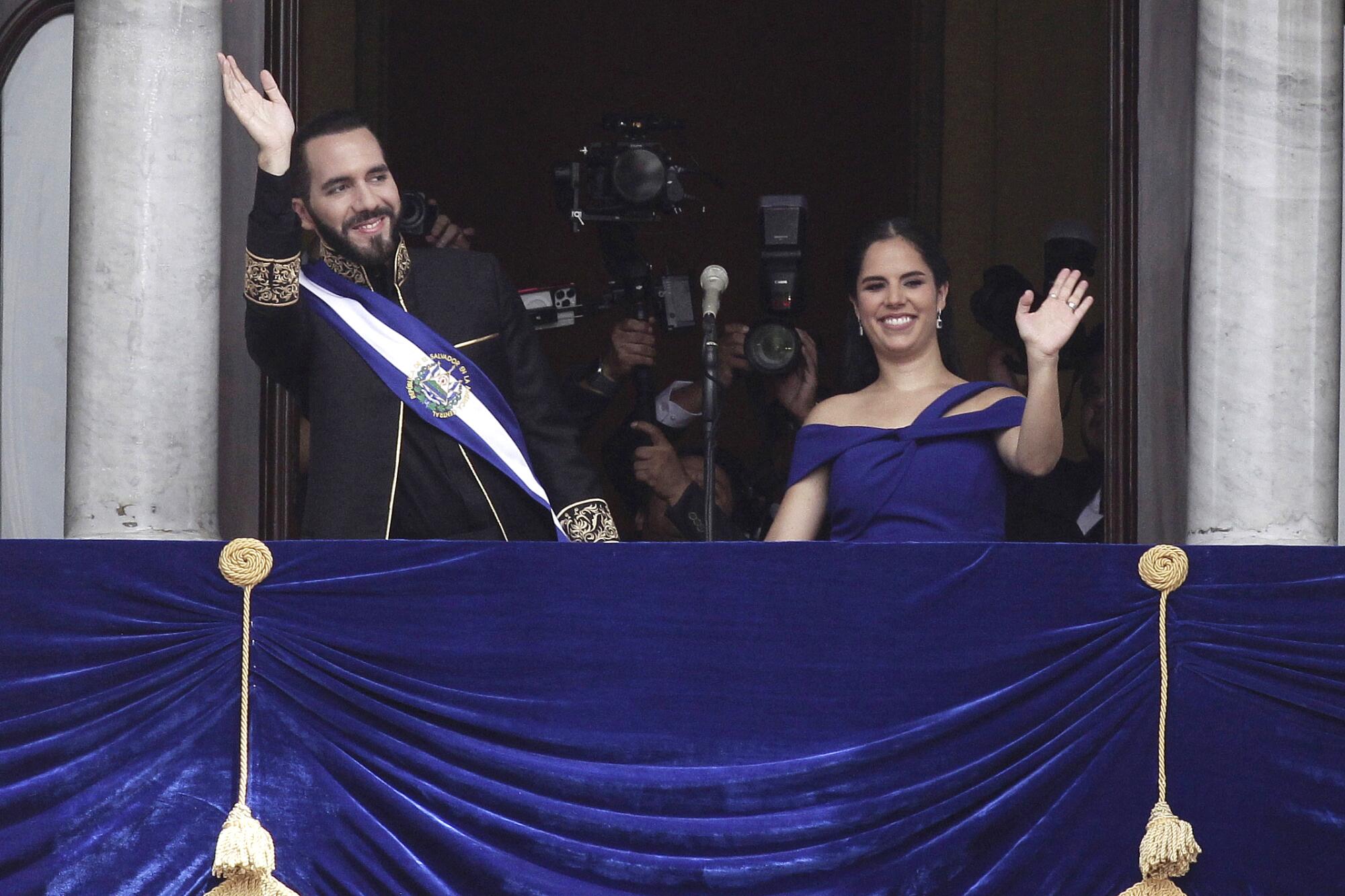 El Salvador's President Nayib Bukele and first lady Gabriela Roberta Rodríguez wave from a draped balcony.