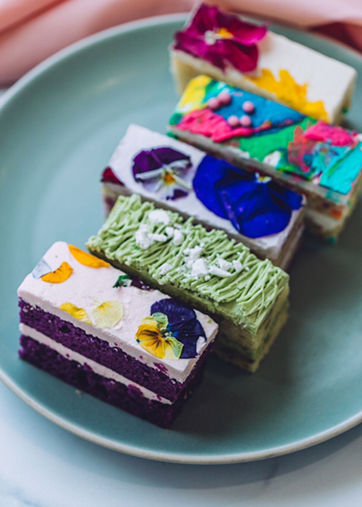 A vertical photo of colorful and flower-topped cake bars side by side on a plate.