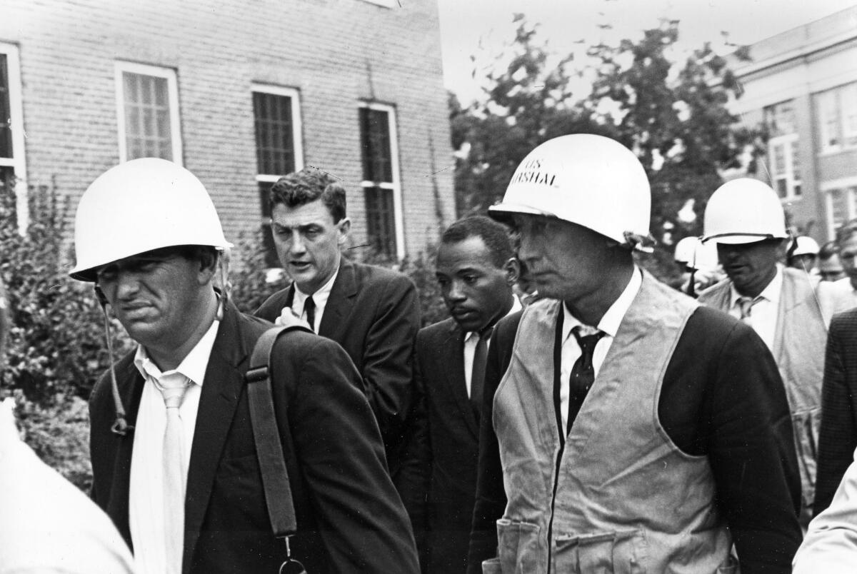 A black-and-white photo of James Meredith, center, being escorted by federal marshals, some wearing helmets. 