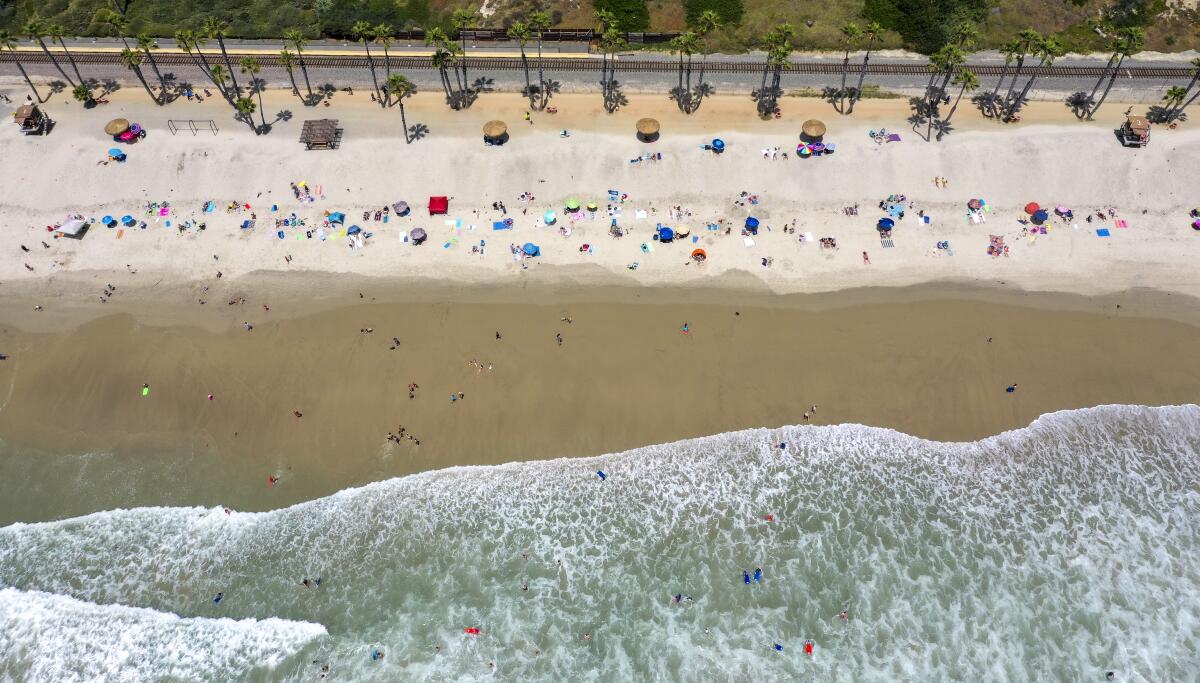  An aerial view of beach-goers taking to the water on a warm summer day at the San Clemente Pier on Tuesday, June 30, 2020.  