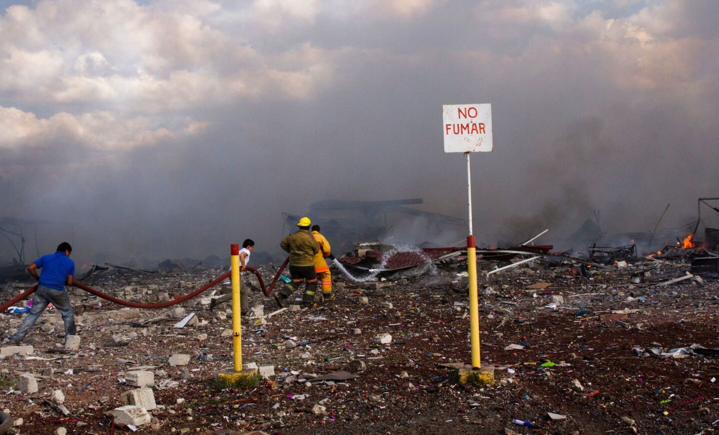 Firefighters work amid the smoldering debris left by explosions at a fireworks market north of Mexico City.