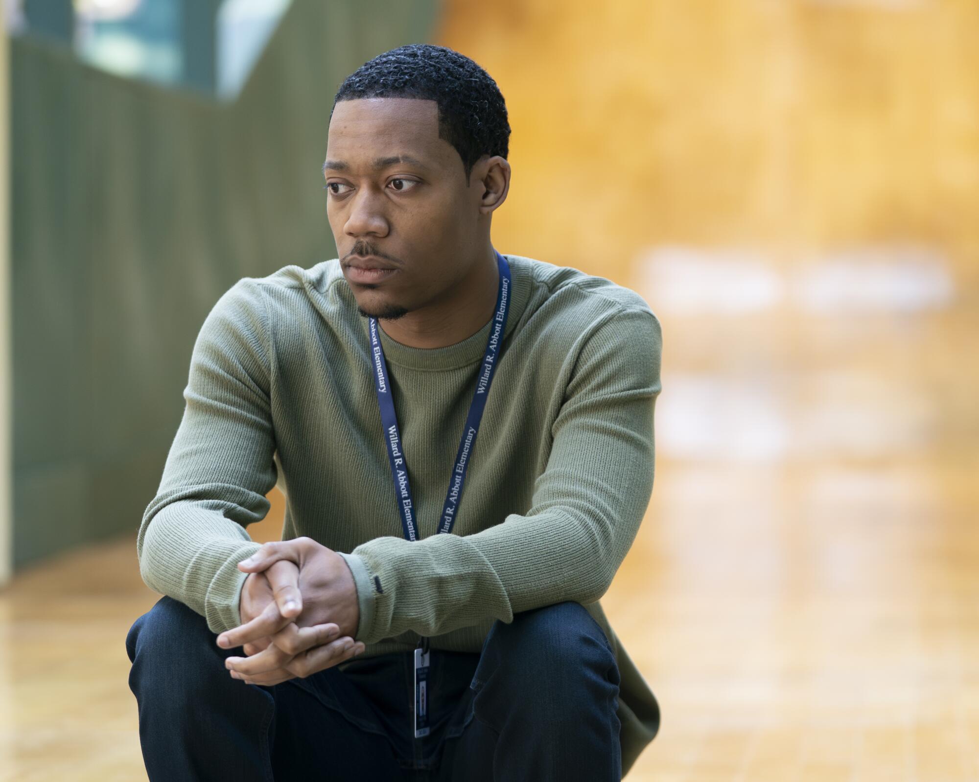 A young man squats, looking pensive.