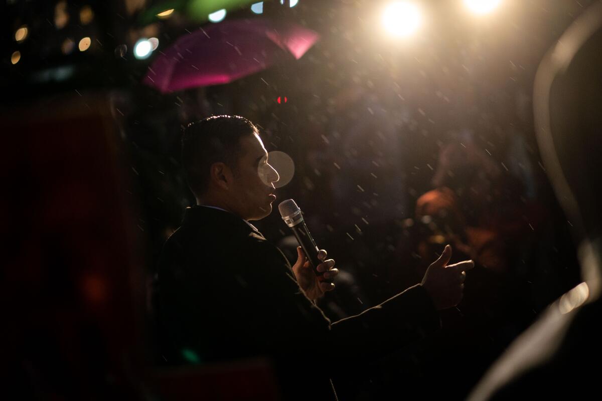 A man, seen from the side, holds a microphone while speaking in the rain 