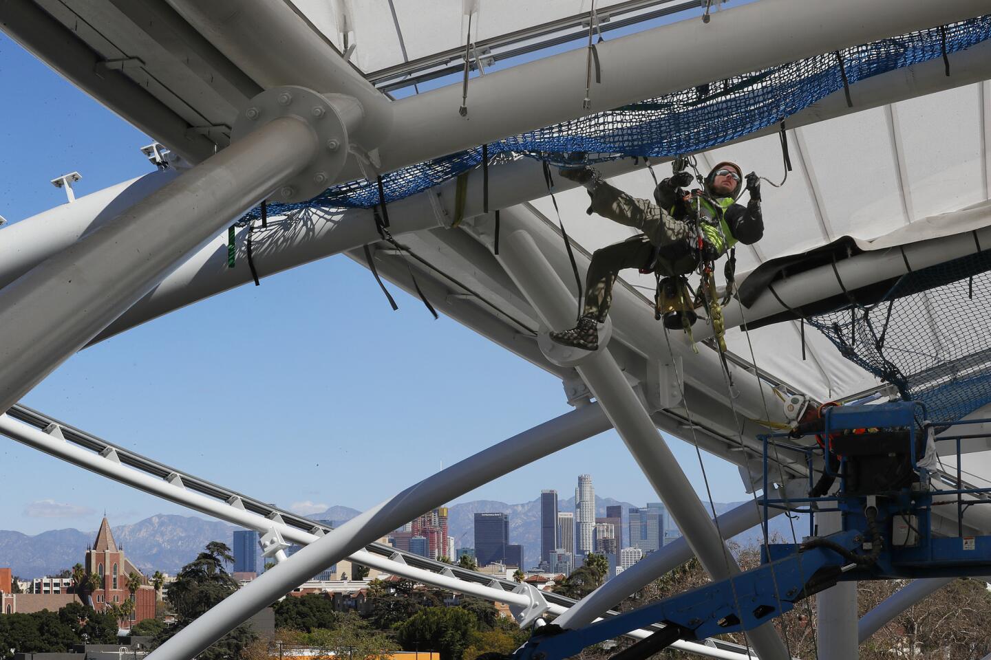 A construction worker rappels from the roof structure to secure the safety netting and install roof panels of LAFC's new Banc of California Stadium on Feb. 22.