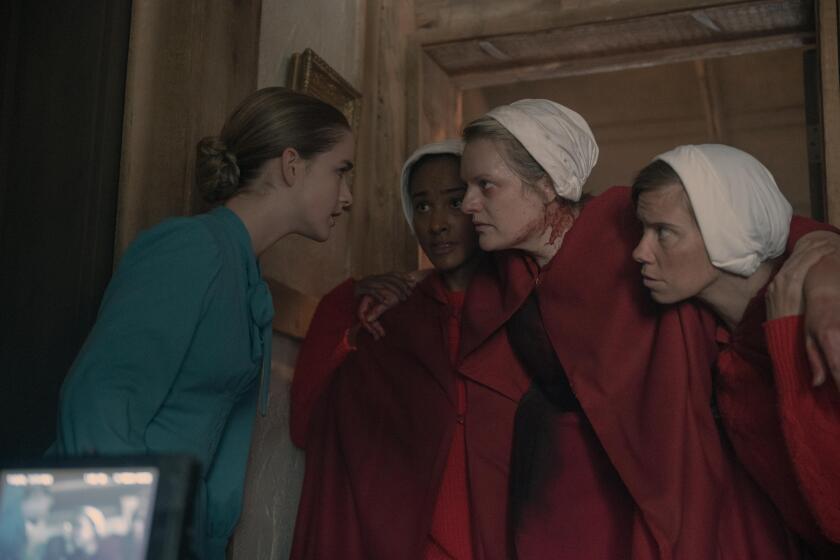 A woman in blue leans in to speak to an injured woman in red being carried by two others. 
