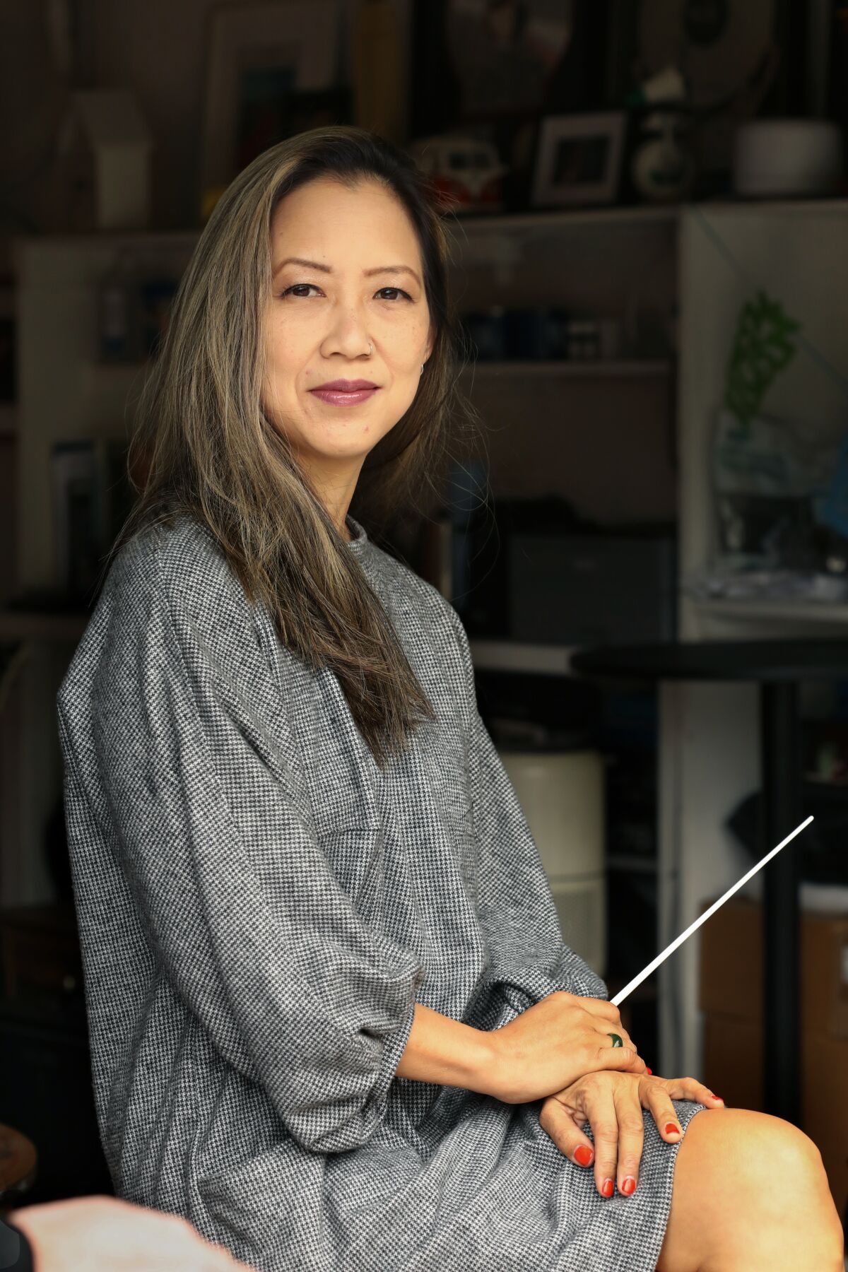 A woman holds a conductor's baton and poses for a photo.