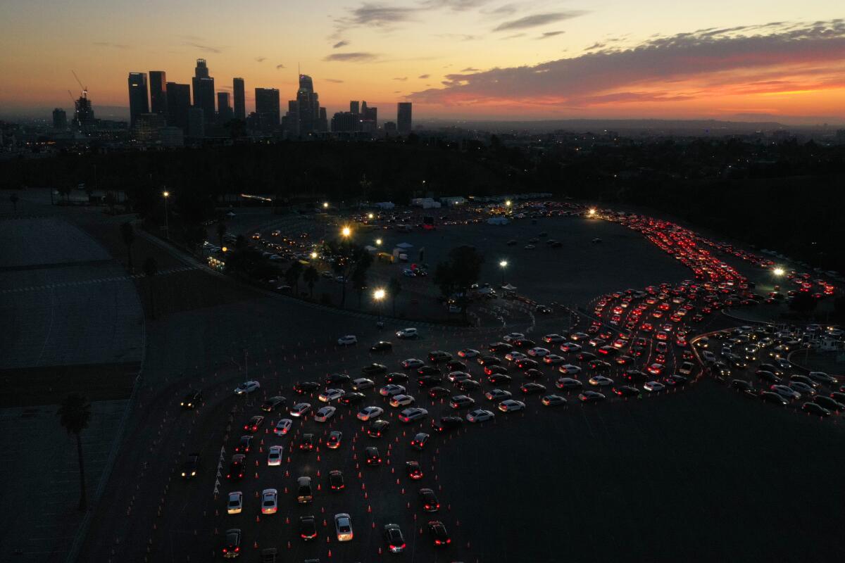 Snaking lines of car taillights six lanes wide at dusk, with the downtown L.A. skyline in the background