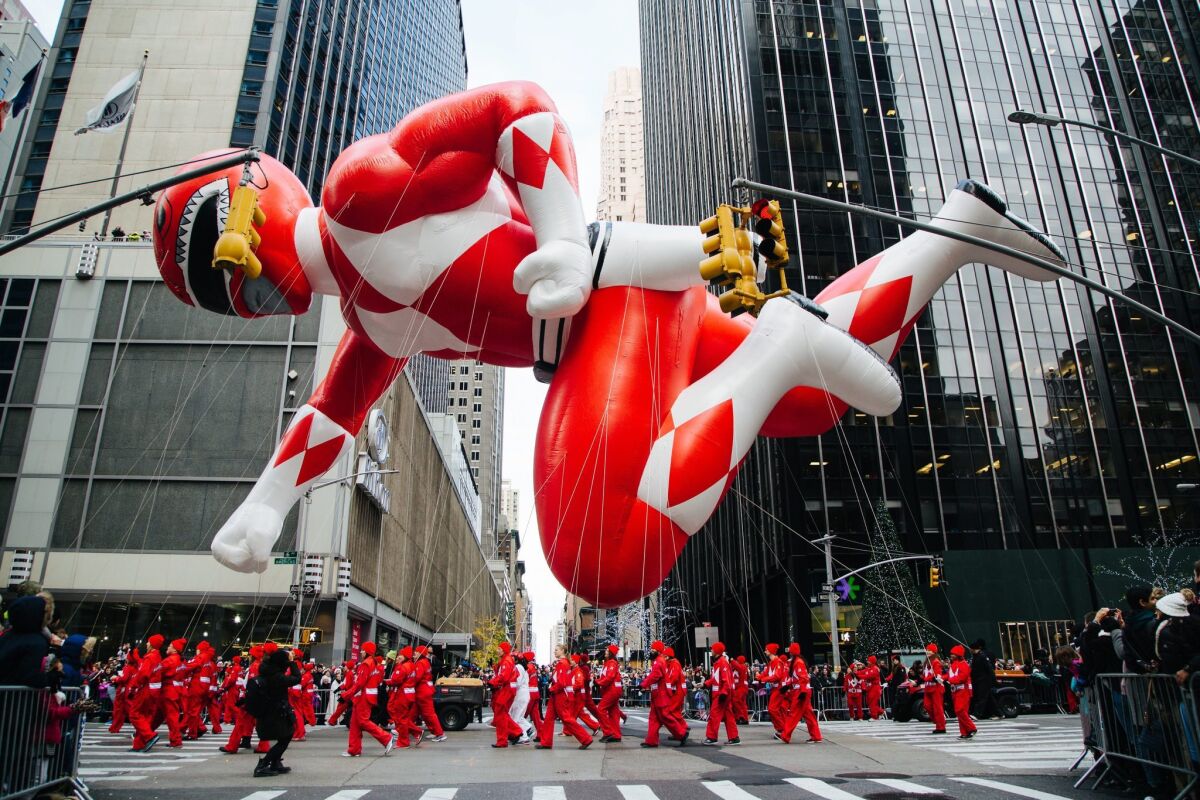 Amid skyscrapers, a Power Ranger balloon floats, dwarfing parade participants on the street.