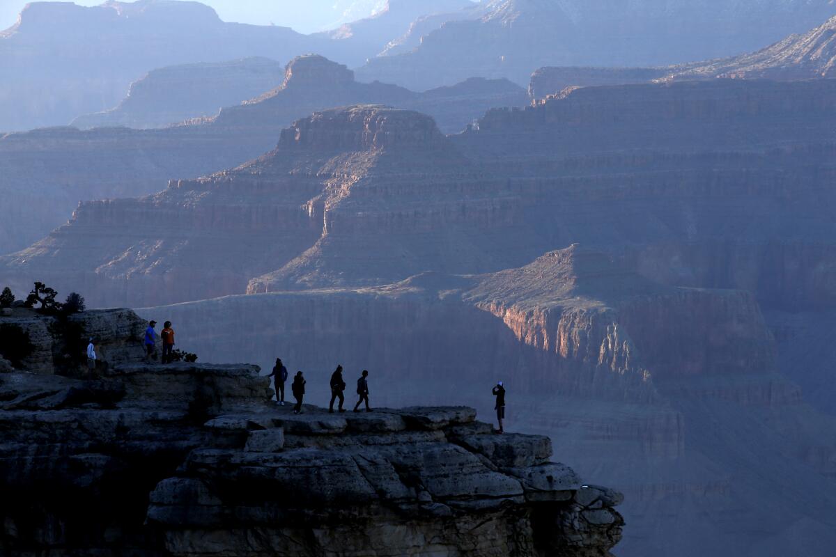 People stand on a point silhouetted by the Grand Canyon