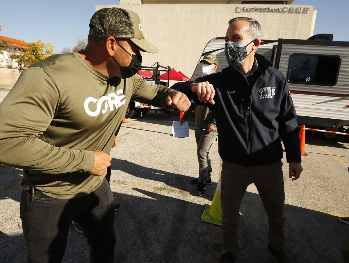 L.A. Mayor Eric Garcetti, right, greets a man at a mobile COVID-19 vaccination clinic.