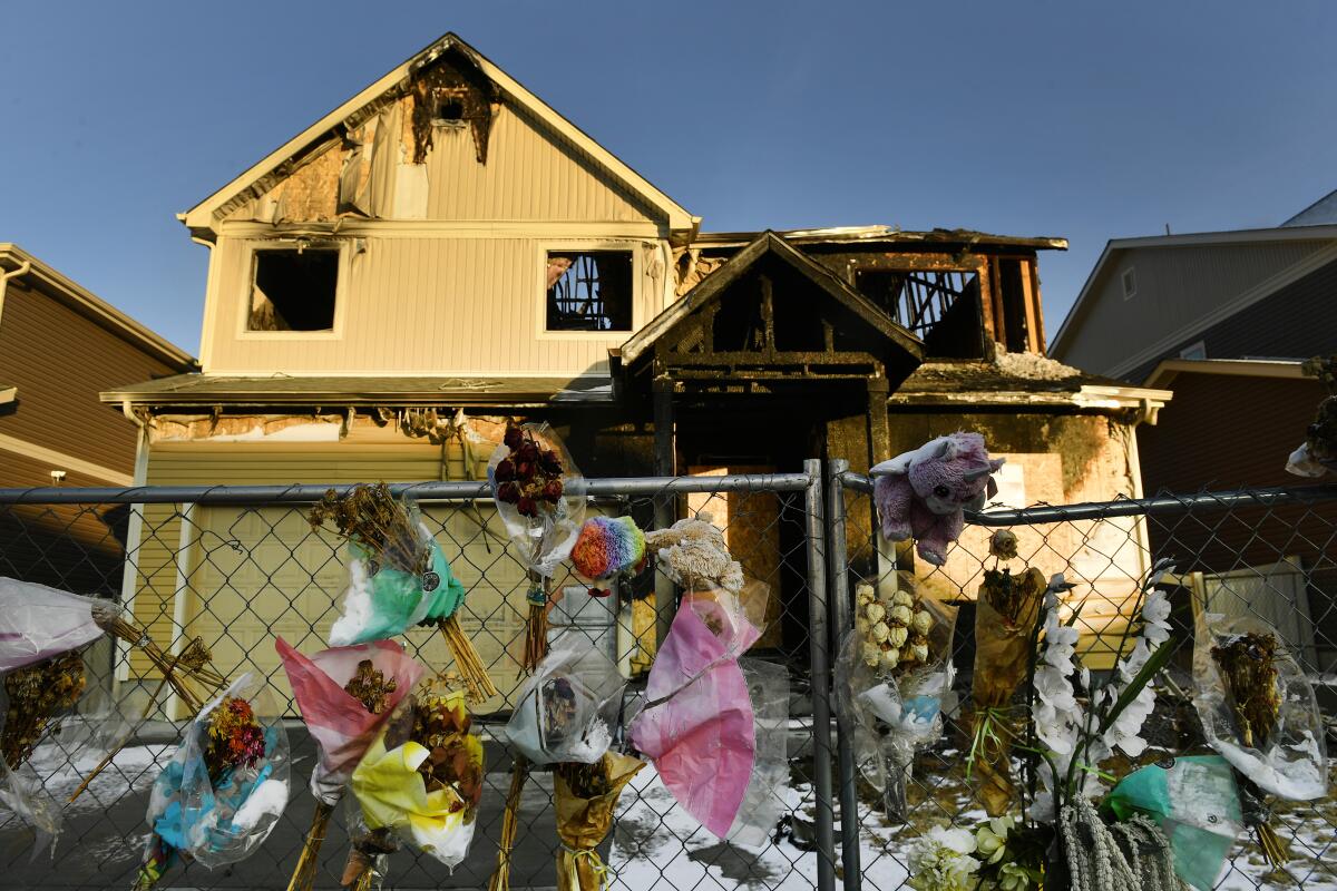 A house where five people were killed in a fire is surrounded by bouquets, stuffed animals and other remembrances.