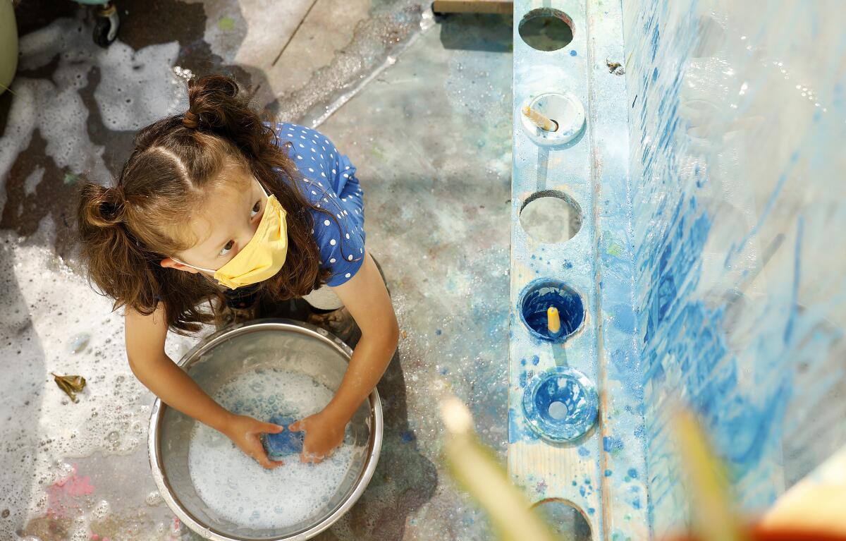 A child wears a mask while painting at a preschool in Los Angeles. 