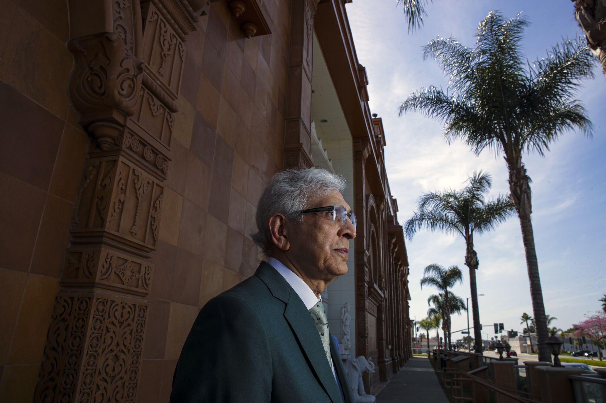 A man in a suit stands on the sidewalk outside a Jain temple