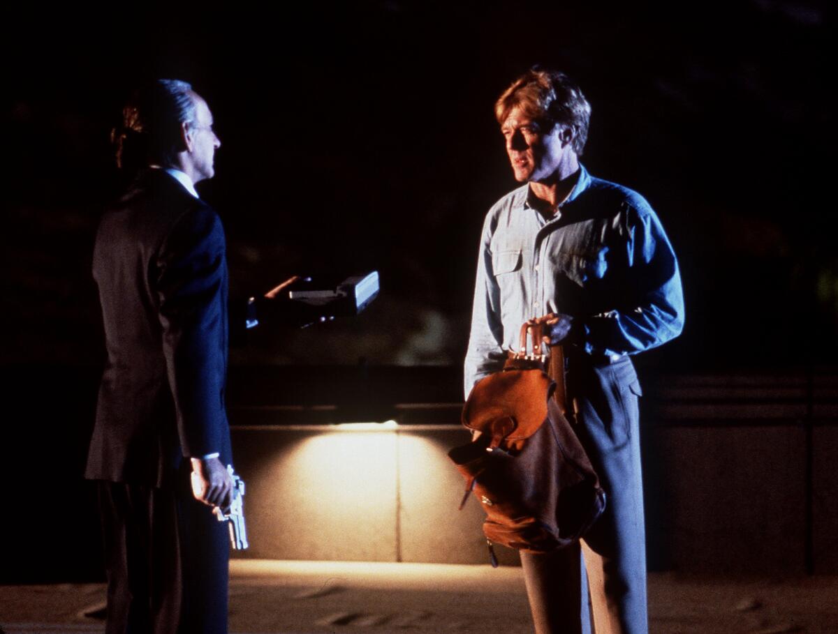 Two men have a stealthy spy conversation in the shadows.