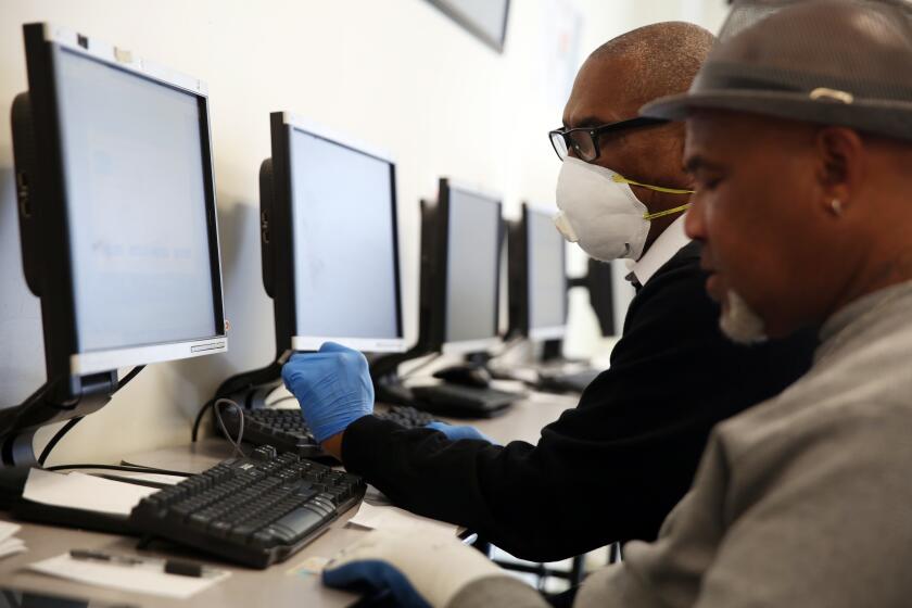 LOS ANGELES, CA-MARCH 26, 2020: Stanley Smith, left, with South L.A. WorkSource Center helps Gregory Allen, right, in the computer lab with job finding services on March 26, 2020 in Los Angeles, California. The number of Americans applying for jobless benefits soared to unprecedented levels last week as new government data put into stark relief the magnitude of the economic pain caused by the coronavirus outbreak. (Photo By Dania Maxwell / Los Angeles Times)
