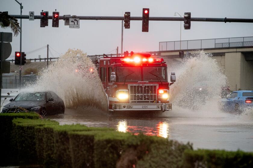 COACHELLA, CA - AUGUST 20, 2023: A Riverside County fire engine blasts through flood waters creating rooster tails which cover two cars stuck in the flood water on Avenue 48 during tropical storm Hilary on August 20, 2023 in Coachella, California. (Gina Ferazzi / Los Angeles Times)