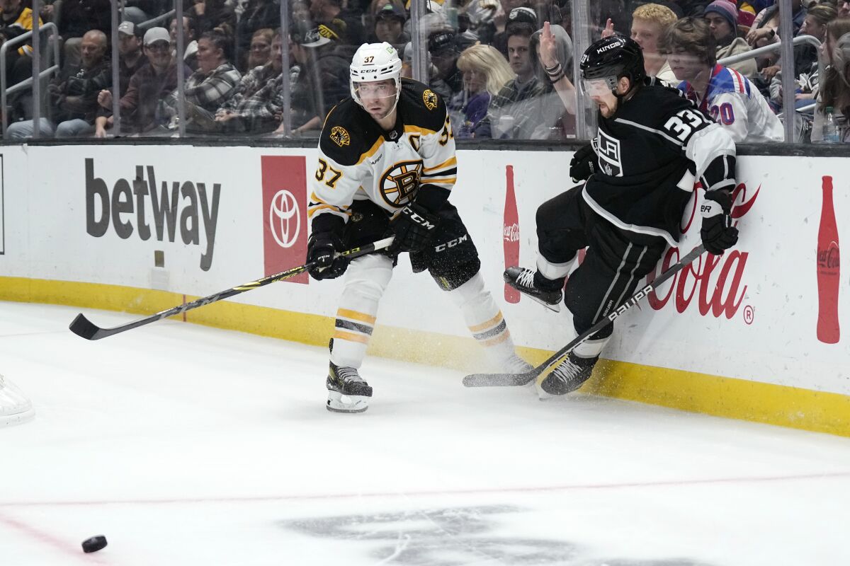 Boston Bruins center Patrice Bergeron passes the puck as Kings right wing Viktor Arvidsson runs into the boards.