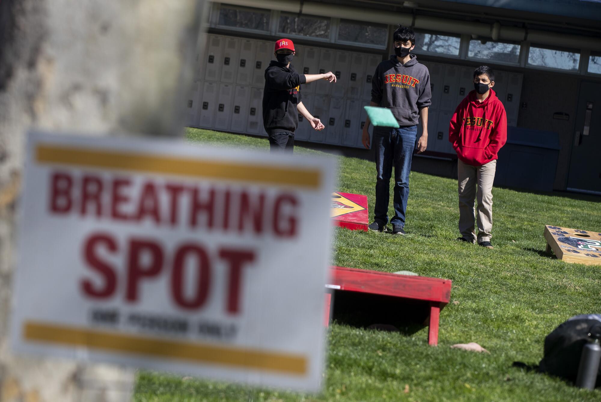 High school students toss cornhole bags in a lawn next to a sign that says Breathing Spot