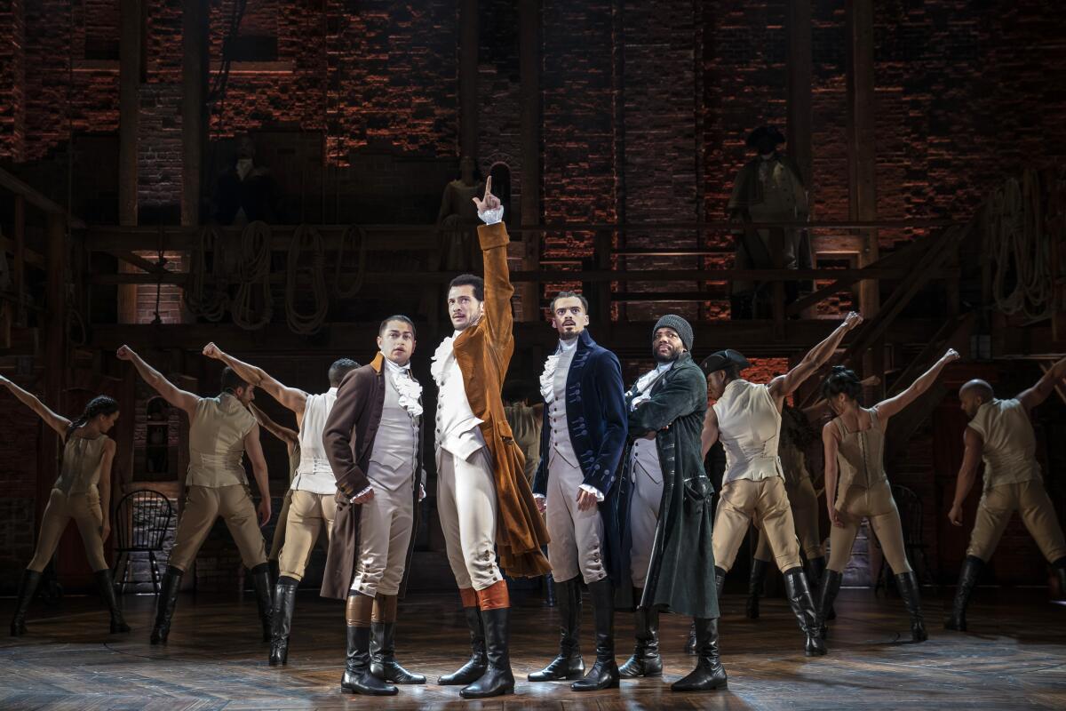 Men onstage stand in a v-shape in colonial clothing