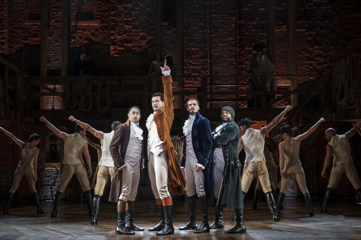 Men onstage stand in a v-shape in colonial clothing 