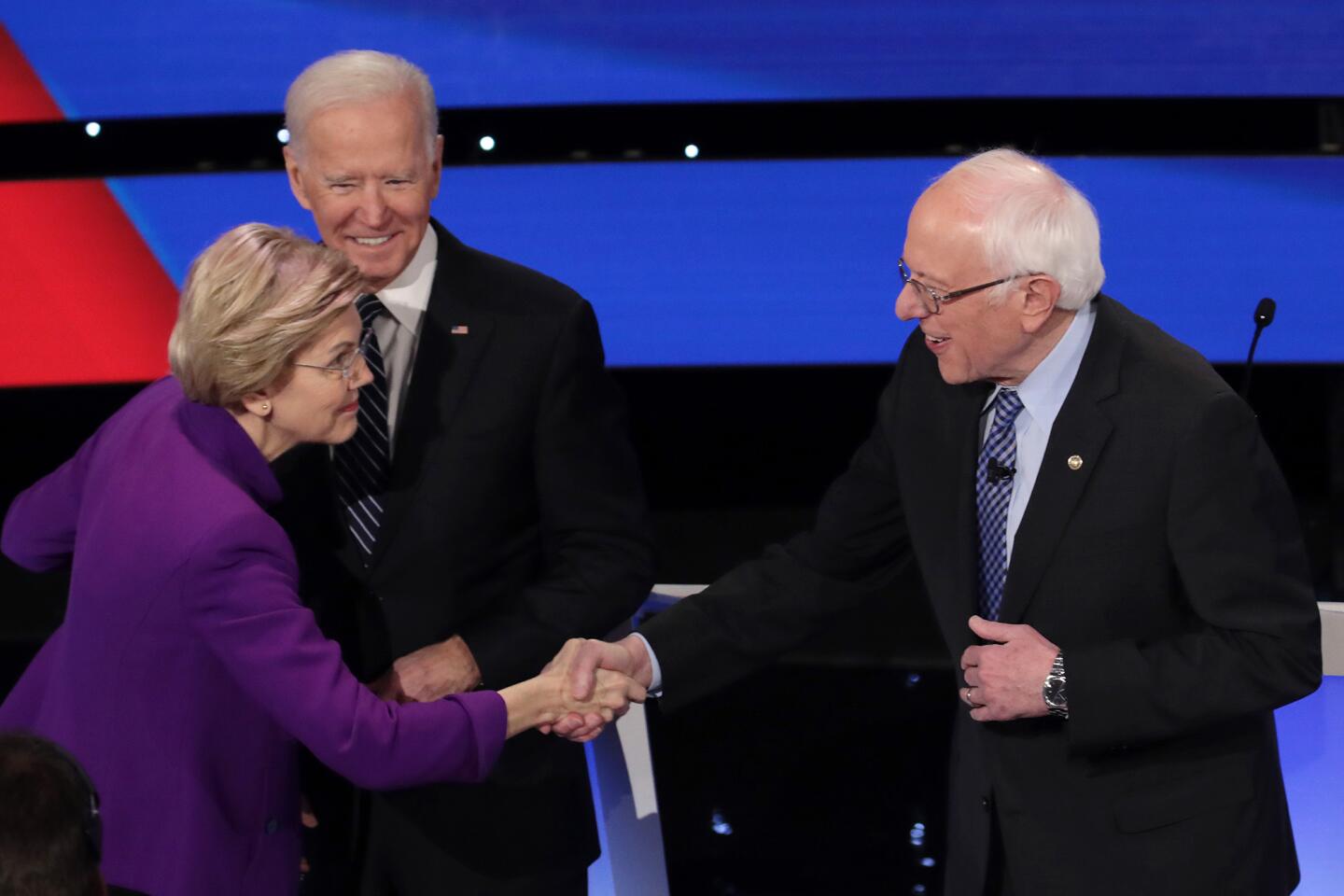 Elizabeth Warren greets Bernie Sanders as Joe Biden looks on.