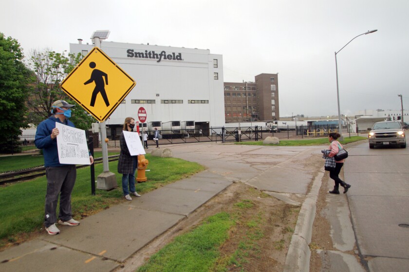 FILE - In this May 20, 2020, file photo, residents cheer and hold thank you signs to greet employees of a Smithfield pork processing plant as they begin their shift in Sioux Falls, S.D. Workers at the South Dakota meatpacking plant that became a coronavirus hotspot last year are considering a strike after contract negotiations between Smithfield Foods and the union have stalled, the union said Wednesday, June 2, 2021. (AP Photo/Stephen Groves, File)