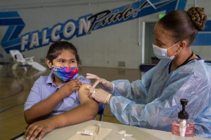 SAN FERNANDO, CA - AUGUST 30, 2021: Tracy Jones, a licensed vocational nurse, places a bandage on the arm of Angel Macias, 12, a 7th grader at San Fernando Institute for Applied Media in San Fernando, after giving the student the first dose of the Pfiizer vaccine. A mobile COVID-19 vaccine clinic was set up inside the gymnasium at San Fernando Middle School to inoculate LAUSD employees and students age 12 and older. (San Fernando Institute for Applied Media is located on the San Fernando Middle School campus) (Mel Melcon / Los Angeles Times)