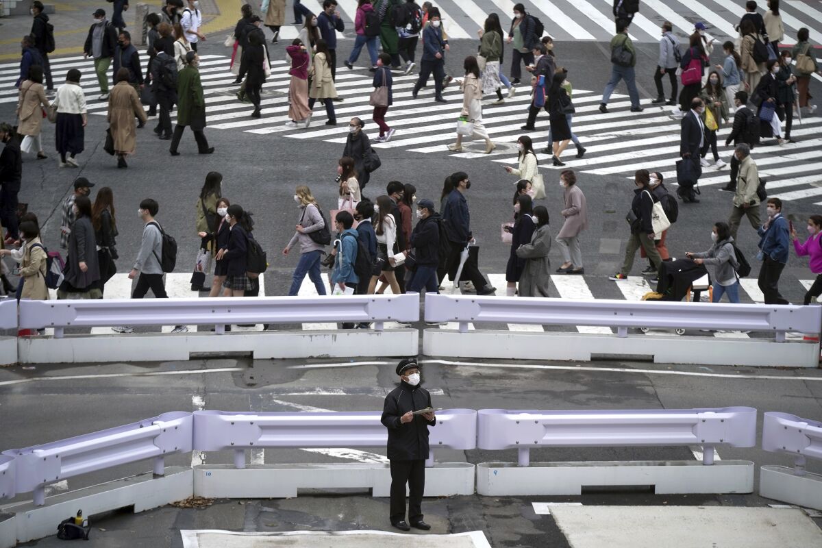 FILE - People wearing protective masks to help curb the spread of the coronavirus walk along a pedestrian crossing on April 20, 2022, in Tokyo. Japan’s economy shrank at an annual rate of 1% in the first quarter, as rising prices and COVID-19 restrictions deadened spending and investment, according to data released Wednesday, May 18 2022.(AP Photo/Eugene Hoshiko, File)