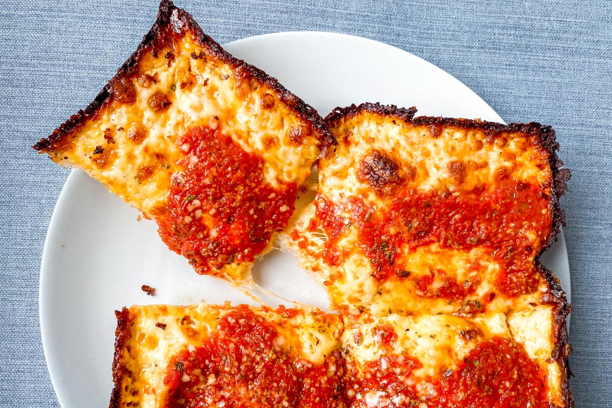 Close-up of a white plate with squares of thick pizza charred on the edges, with red sauce on top of the cheese.
