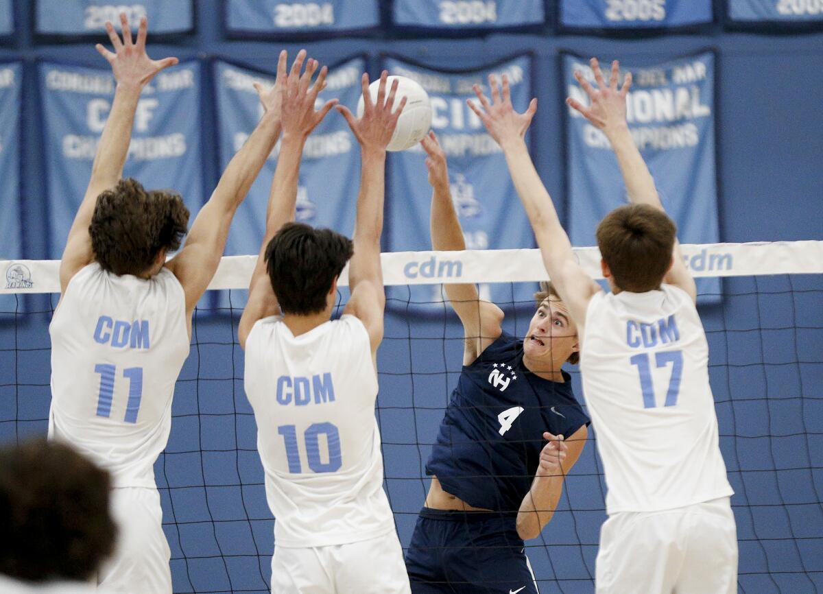 Newport Harbor outside hitter Luca Curci (4) hits into a wall of Corona del Mar blockers during a boys' volleyball match.