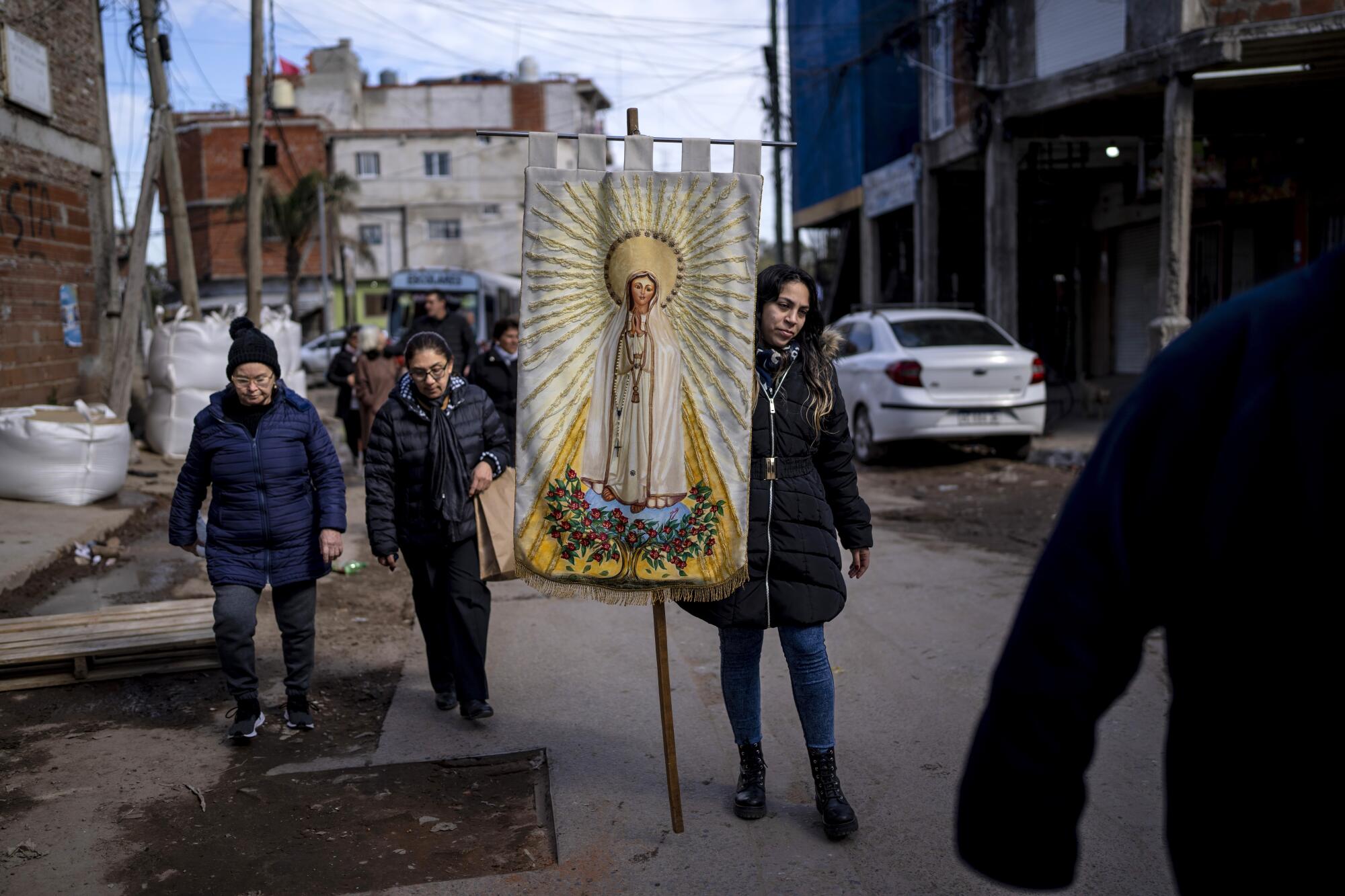 People walk down a street, on of them carrying an image of a religious icon