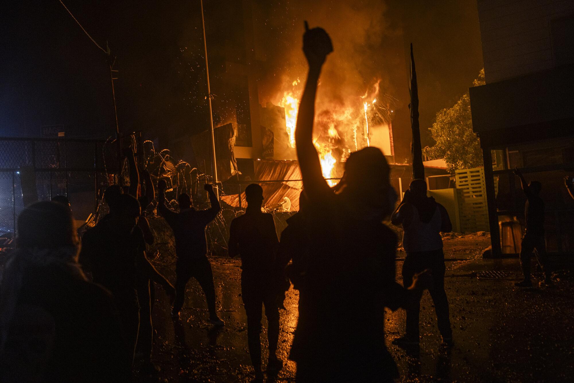 Demonstrators silhouetted at night in front of flames in the distance.
