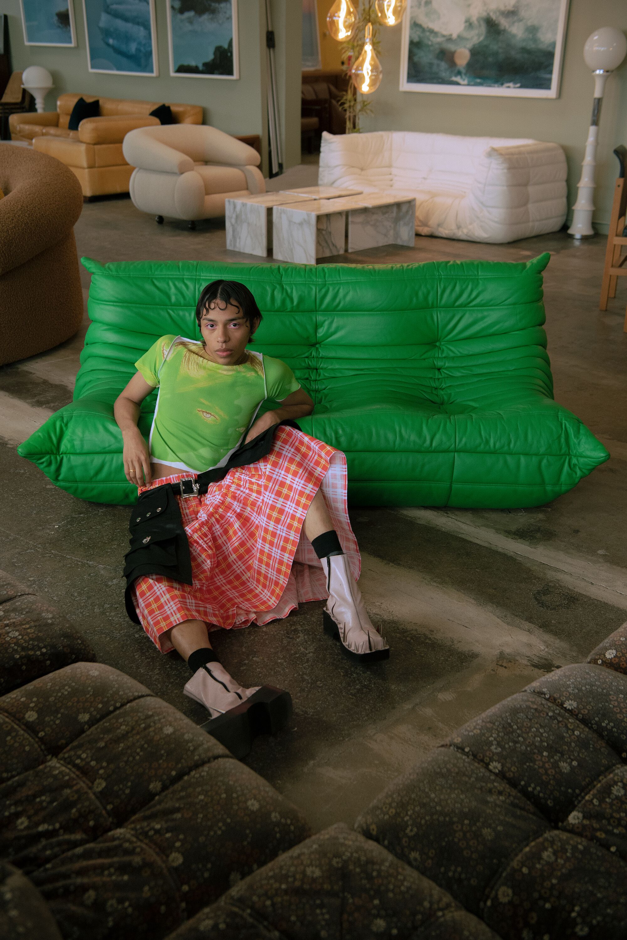 Una modella sdraiata a terra appoggiata su un divano verde brillante.