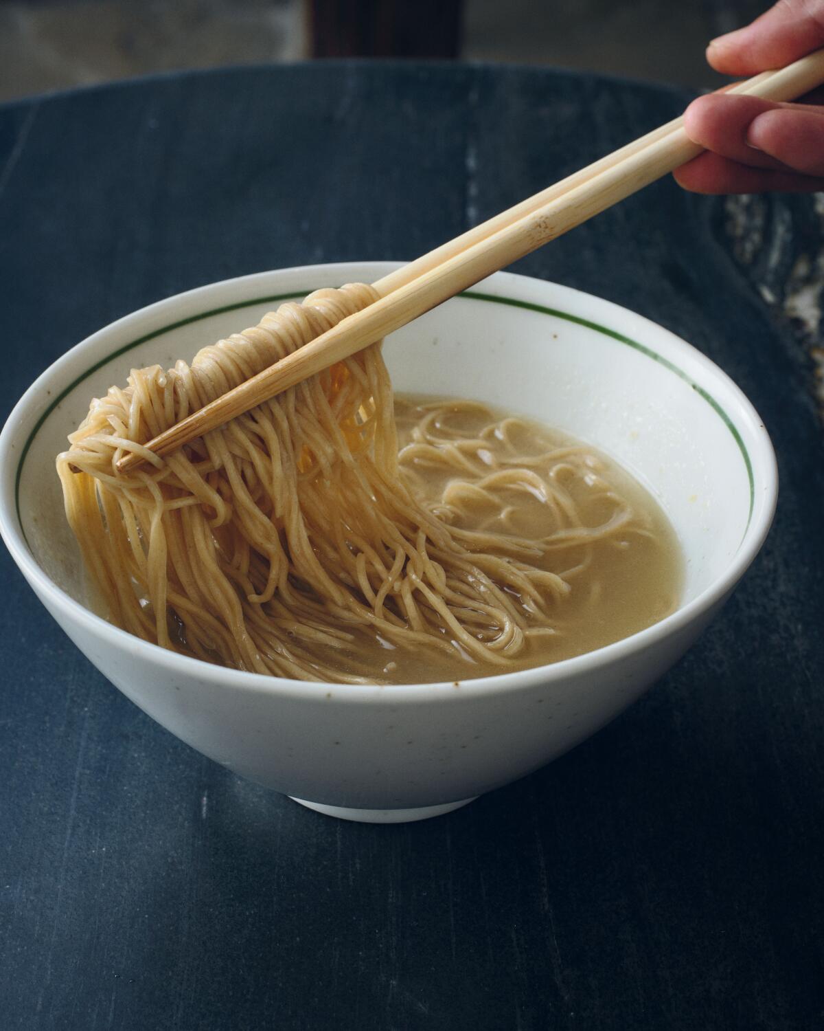 Chopsticks lift house-made ramen noodles from a bowl of yellow broth at RVR in Venice.