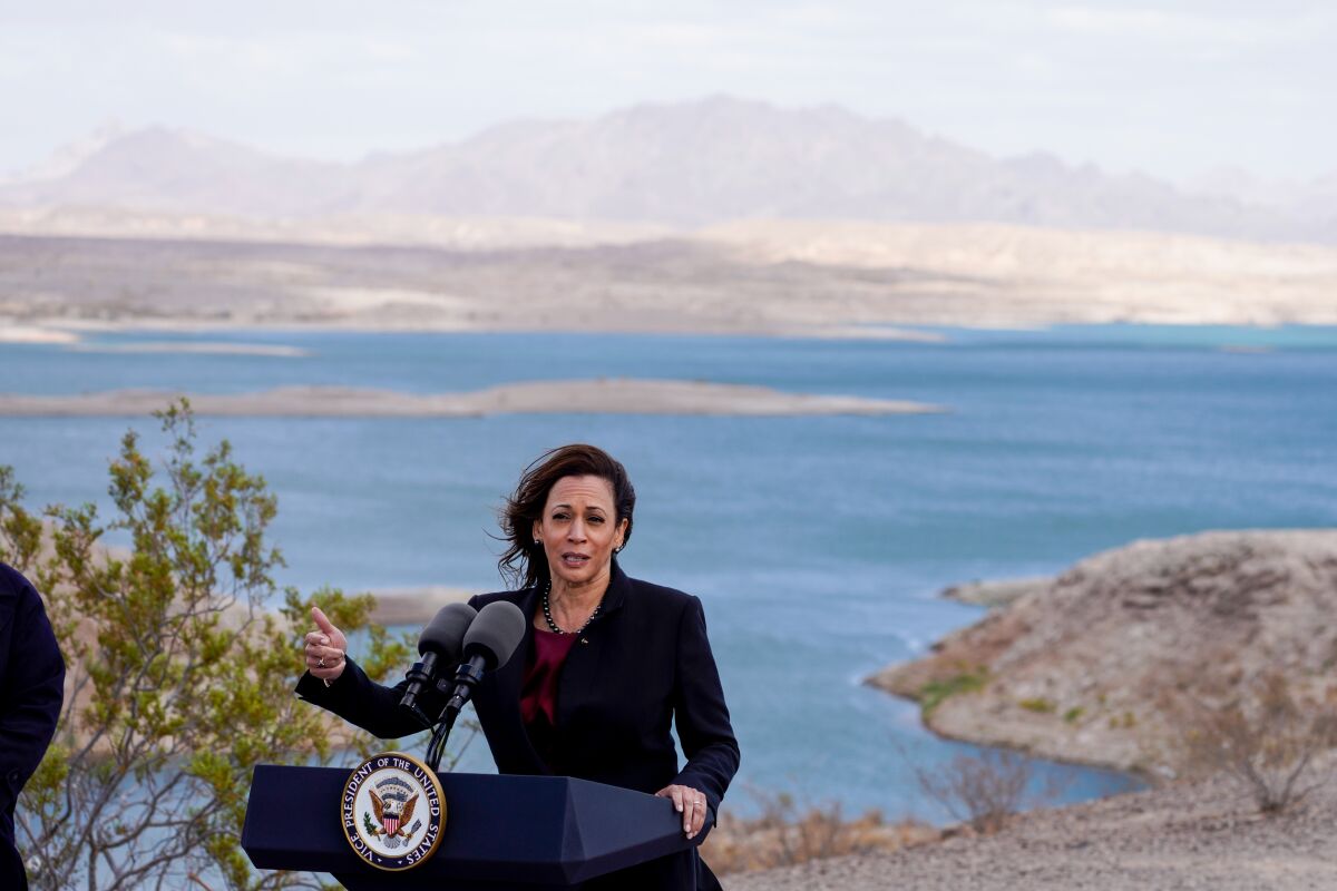 A woman gestures as she stands before a lectern with the U.S. vice presidential seal in front of a lake 