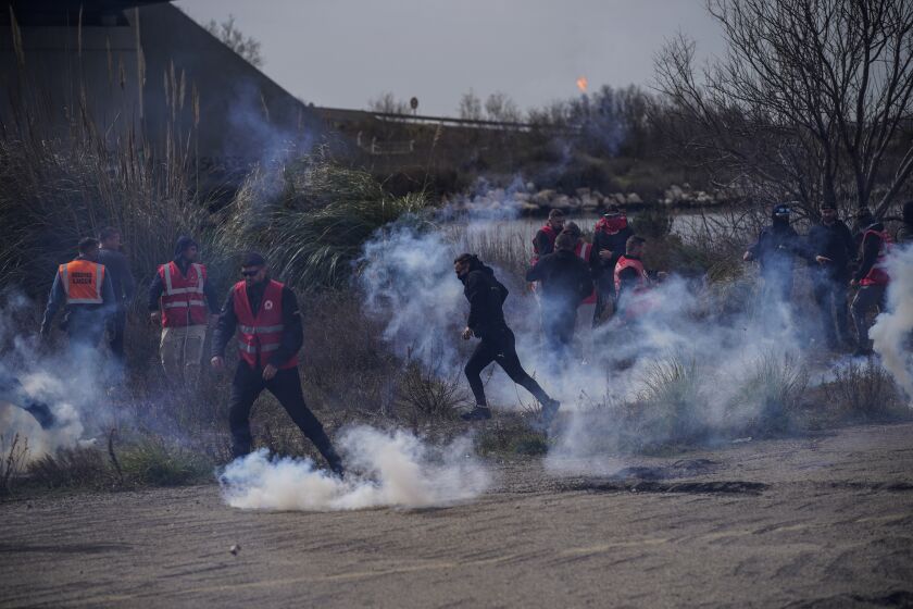 Oil workers run from tear gas fired by French riot police as they block the access to an oil depot in Fos-sur-Mer, southern France, Tuesday, March 21, 2023. The bill pushed through by President Emmanuel Macron without lawmakers' approval still faces a review by the Constitutional Council before it can be signed into law. Meanwhile, oil shipments in the country were disrupted amid strikes at several refineries in western and southern France. (AP Photo/Daniel Cole)