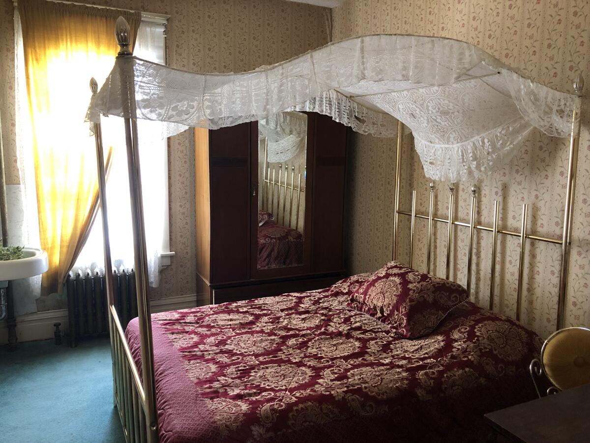 A small room with flowered wallpaper and a brass bed with lace canopy.