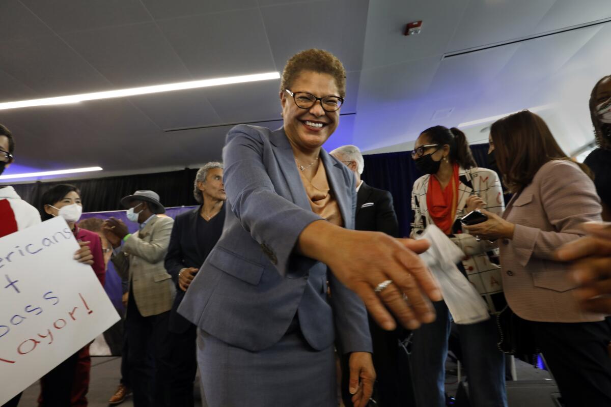 Mayor Karen Bass in a light purple suit stretches out her hand for someone to shake it
