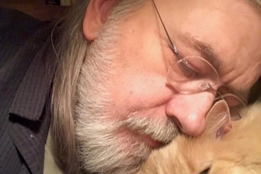 Caleb Carr, with glasses and a white beard, nestles his face on his cat Masha's head.