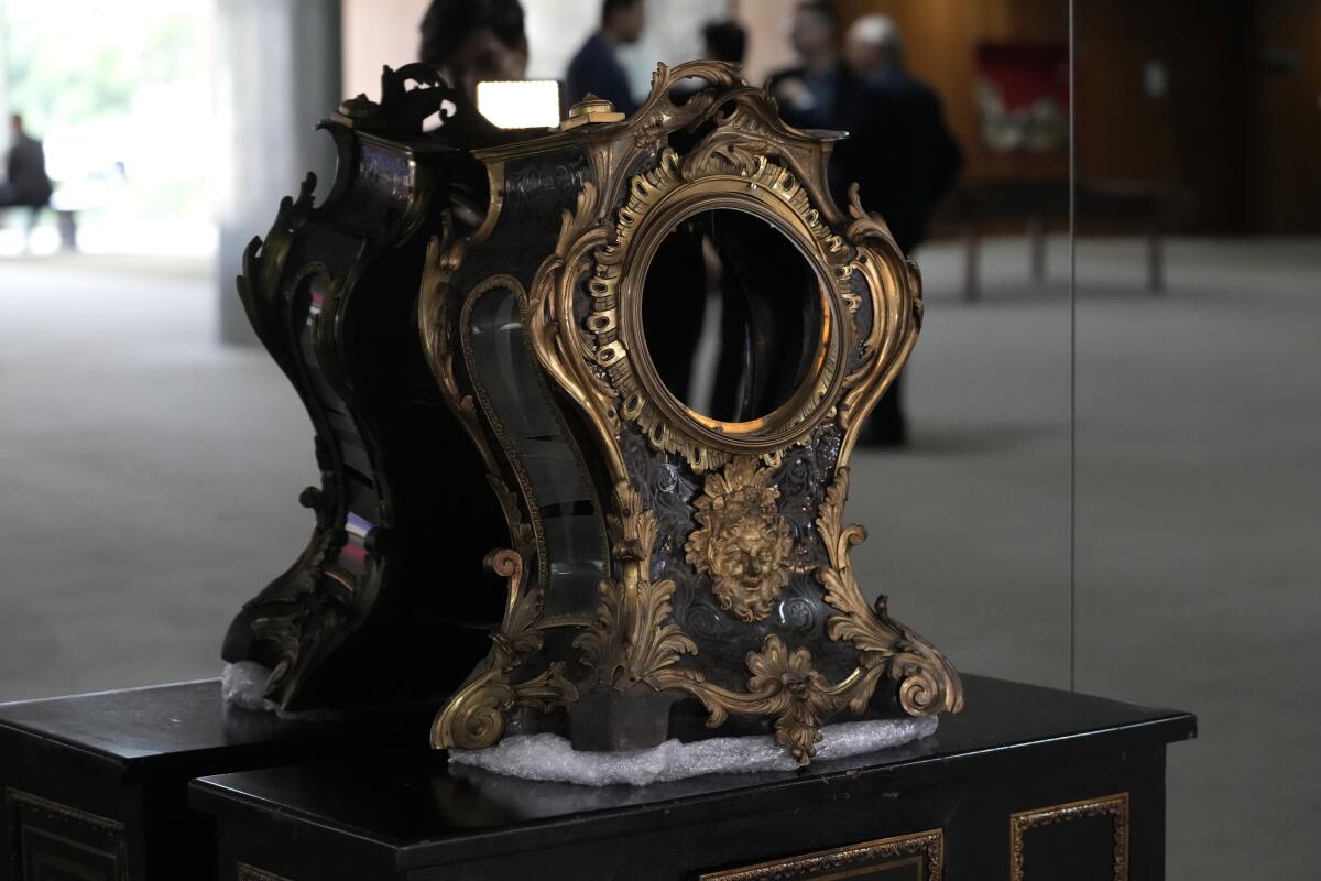 A damaged 17th century clock sits atop a table in front of a mirror