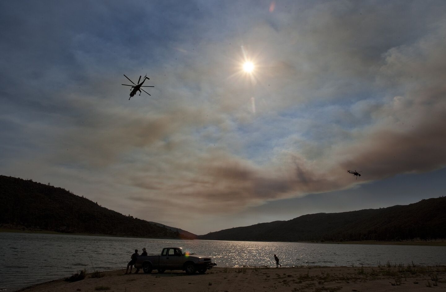 Orange hazy smoke fills the air above Lake Hemet as a water-dropping helicopter uses the lake to refill during the Mountain fire off Highway 74 at Mt. San Jacinto State Park.