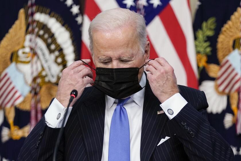 President Biden fixes his face mask Monday at a White House meeting