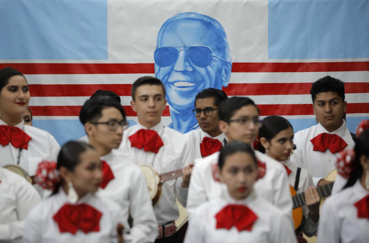 Members of a mariachi band stand in front of a banner with an image of President Biden wearing sunglasses.