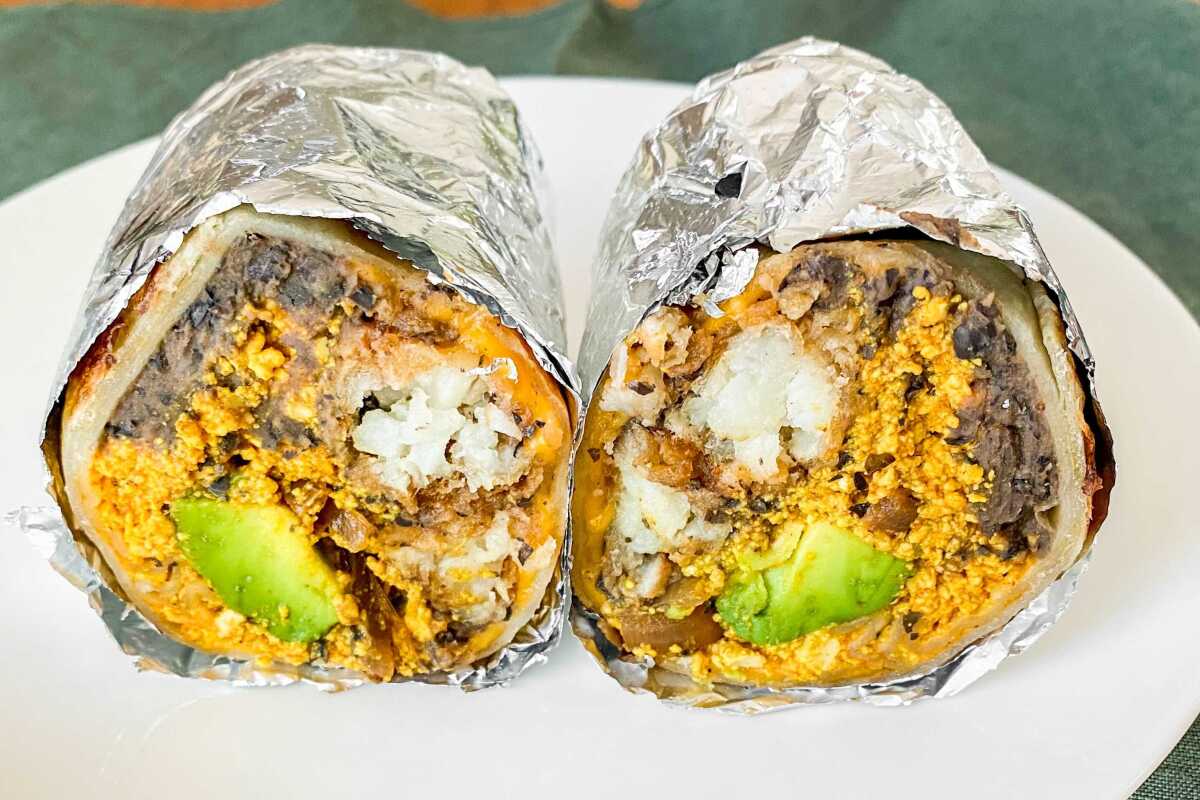 Vegan burrito with scrambled tofu and refried black beans, wrapped in foil and cut in half, open to the camera