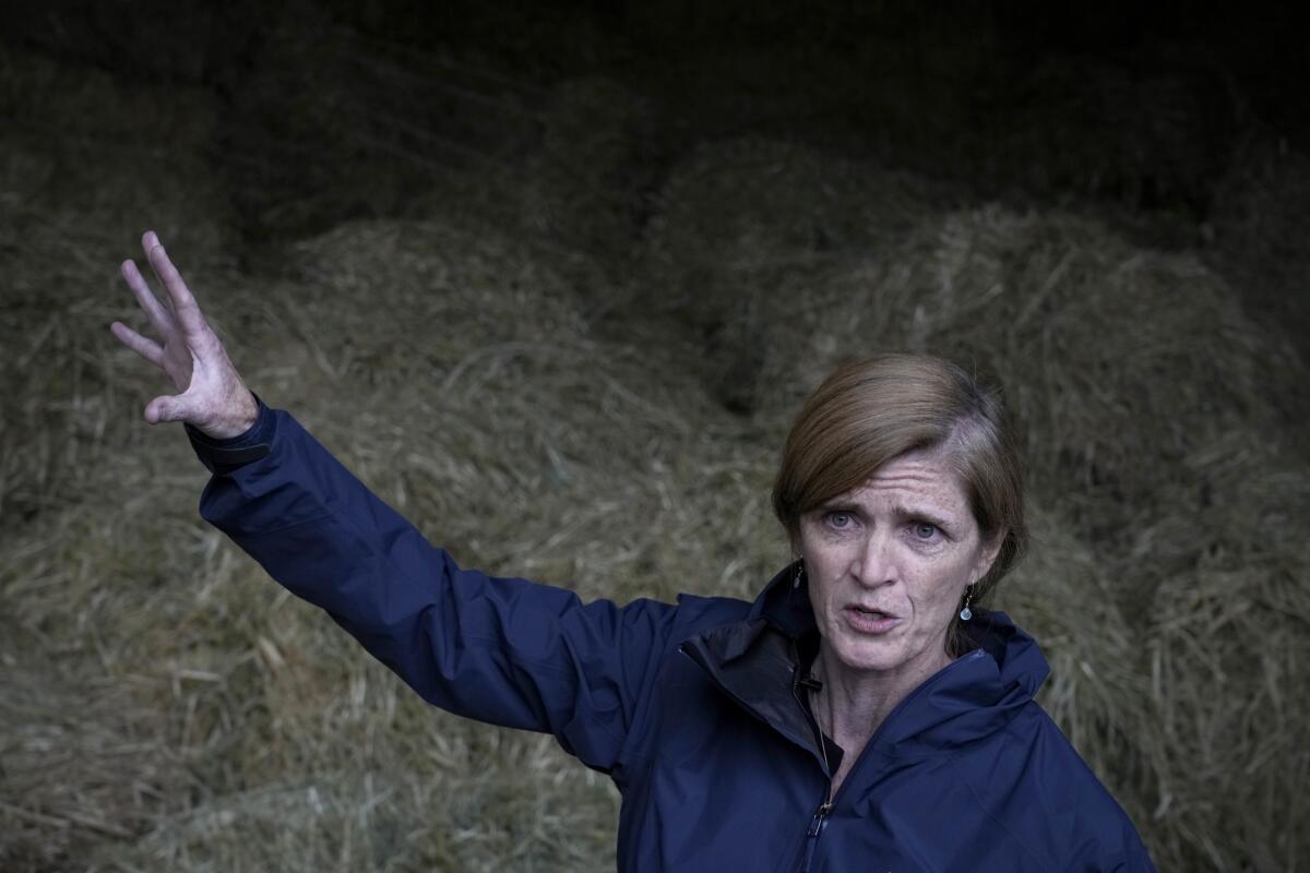 A woman pictured from the shoulders up in front of piles of animal feed, gesturing as she speaks